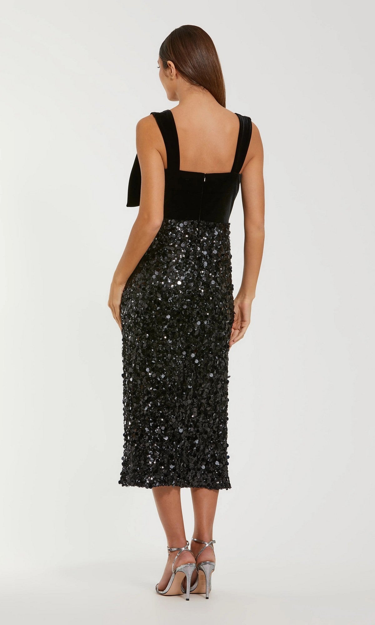 A woman stands with her back to the camera, modeling the Mac Duggal 27777 midi semi-formal dress with sequin details and silver high-heeled sandals against a plain white background.